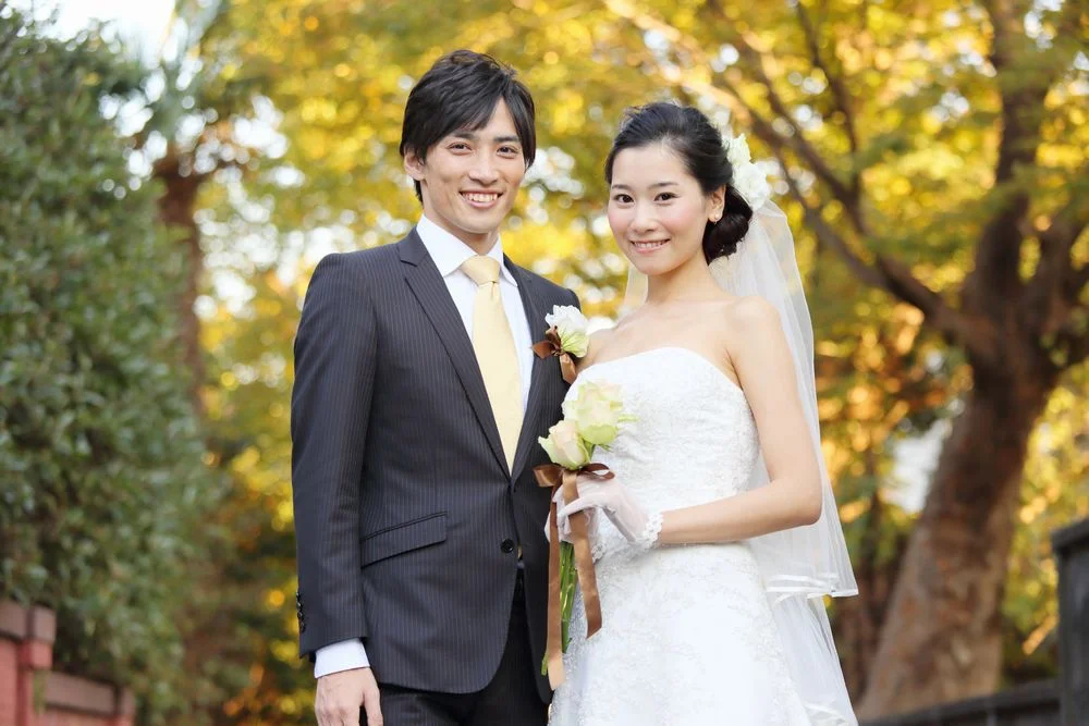 紅葉を背景に、ブーケを手にして微笑むウェディング姿の男女